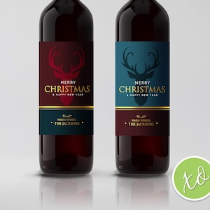 Puede incluir: Dos botellas de vino con etiquetas navideñas festivas que presentan una silueta de reno. Las etiquetas son rojas y azules con detalles dorados. El texto en las etiquetas dice "Feliz Navidad y Feliz Año Nuevo" y "Saludos cordiales, Los Jackson".