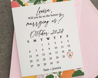 Puede incluir: Una tarjeta blanca con un borde floral y el texto "Louise, ¿Quieres hacernos el honor de casarte con nosotros?" con un calendario de octubre de 2024 con el 26 marcado en rojo.