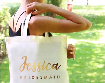May include: A white canvas tote bag with gold lettering that says "Jessica Bridesmaid".