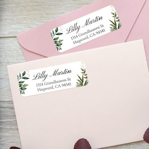 Peut inclure: Deux étiquettes d'adresse blanches avec le nom "Lilly Martin" et les coordonnées, ornées d'illustrations botaniques vertes. Les étiquettes sont posées sur des enveloppes rose clair, créant une esthétique douce et élégante.