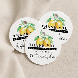 Pode incluir: Três etiquetas de presente circulares brancas com uma ilustração em aguarela de dois limões amarelos com folhas verdes e flores brancas. O texto diz THANK YOU FOR CELEBRATING WITH US e os nomes kristina e john com um coração.