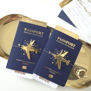 Puede incluir: Invitaciones de boda tipo pasaporte azul marino con detalles dorados, con un dije de avión dorado y los nombres Samantha & Thimothy, con fecha 09.27.2027. Incluye tarjeta de embarque y una bandeja dorada.