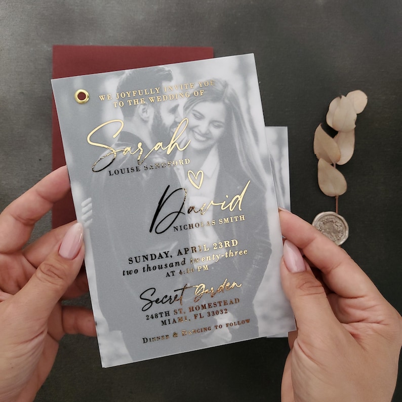 May include: A translucent wedding invitation card featuring a black and white photograph of a couple, accented with gold foil text that reads Sarah Louise Sandford and David Nicholas Smith, Sunday, April 23rd, 2023, at 4:00 PM, Secret Garden.