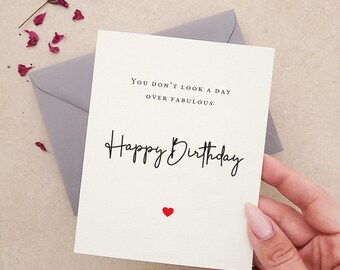 Könnte beinhalten: Eine weiße Karte mit schwarzem Text, der "You don't look a day over fabulous Happy Birthday" lautet, mit einem kleinen roten Herz unten.