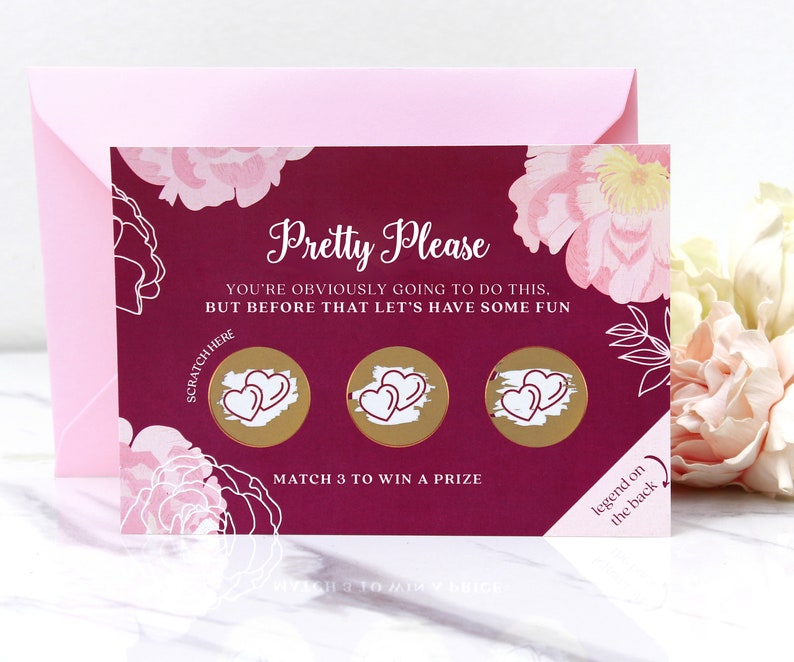 May include: A pink and burgundy card with a floral design. The card has three gold circles with hearts inside. The text on the card reads "Pretty Please You're obviously going to do this. But before that let's have some fun. Scratch here. Match 3 to win a prize. Legend on the back."