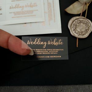Transparent sticker with gold foiled text print. The design features hand-lettered typography spelling out Wedding Website at the top. Below the text reads: visit our website for venue information, accommodation, activities, and more wedding details.