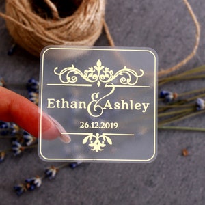 May include: Clear square sticker with gold lettering. The sticker says "Ethan & Ashley" and "26.12.2019".
