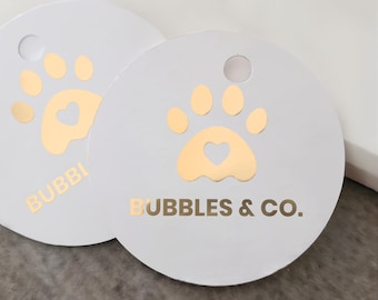 May include: Two white round tags with gold paw print designs and the text "Bubbles & Co.".