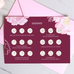 May include: A burgundy card with a floral design and gold accents. The card has a legend with different icons and text, including "Brand New Pair of Garters", "Congrats! Be My Bridesmaid?", "A Date Night With The Groomsmans", "Cheap Bottle of Wine", "Congrats! Be My Maid of Honor?", and "Congrats! Be Our Flower Girl?"