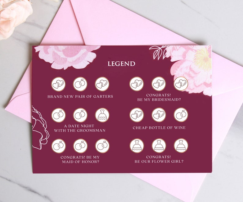 May include: A burgundy card with a floral design and gold accents. The card has a legend with different icons and text, including "Brand New Pair of Garters", "Congrats! Be My Bridesmaid?", "A Date Night With The Groomsmans", "Cheap Bottle of Wine", "Congrats! Be My Maid of Honor?", and "Congrats! Be Our Flower Girl?"