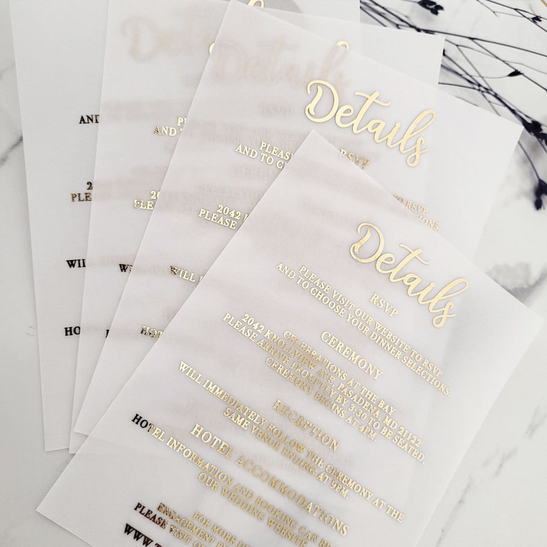 Op de afbeelding: Witte, doorschijnende papieren kaarten met gouden folielettering. De kaarten hebben het woord "Details" erop gedrukt en bevatten informatie over een huwelijksceremonie en een receptie. De tekst bevat de datum, tijd en locatie van de huwelijksgelegenheden.
