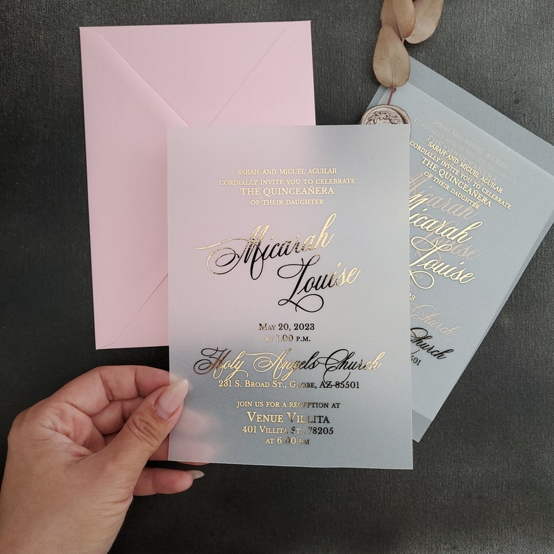 May include: A translucent, light blue and pink invitation card with gold foil lettering. The invitation is for a Quincea&ntilde;era for Micarah Louise. The event will be held at Holy Angels Church on May 20, 2023 at 1:00 p.m. and a reception will follow at Venue Villita at 6:00 p.m.