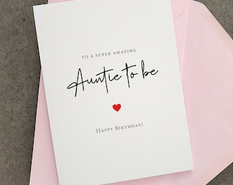 May include: A white greeting card with black text that reads TO A SUPER AMAZING Auntie to be, followed by a small red heart and the text HAPPY BIRTHDAY! The card is placed on top of a light pink envelope, creating a clean and simple presentation.