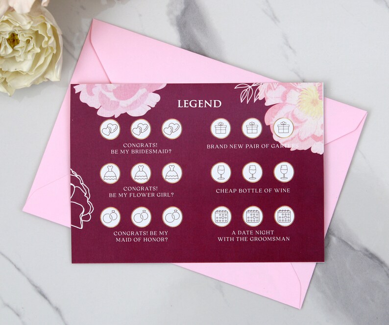 May include: A burgundy card with a floral design and a legend for a bridal shower game. The legend includes icons for a bridesmaid, flower girl, maid of honour, a new pair of garters, a bottle of wine, and a date night with the groomsman.