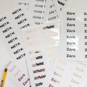 May include: A close-up of a set of personalized name labels. The labels are printed with the names "Matt", "Zara", "Stephanie", and "Oliver". The labels are in various colors, including black, gold, and pink.