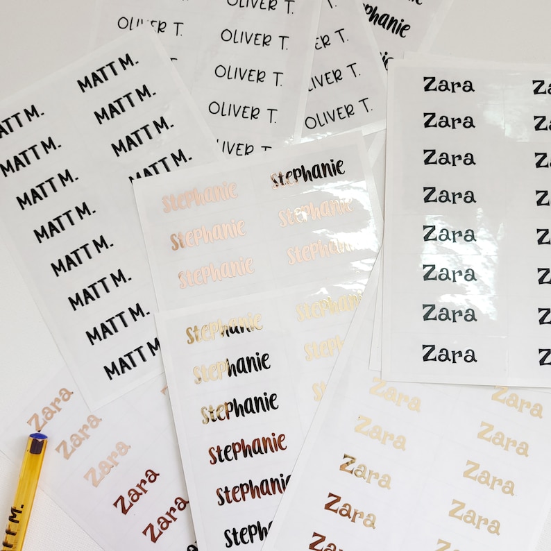 May include: A close-up of a set of personalized name labels. The labels are printed with the names "Matt", "Zara", "Stephanie", and "Oliver". The labels are in various colors, including black, gold, and pink.