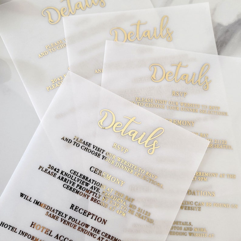 Op de afbeelding: Witte papieren kaarten met gouden folielettering met het woord "Details" en de tekst "RSVP, Bezoek onze website om je aan te melden en je dinerkeuzes te maken." De kaarten bevatten ook de tekst "Ceremonie" en "Receptie".
