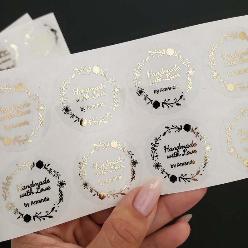May include: A sheet of clear stickers with gold and black lettering. The stickers feature a floral wreath design and the text "Handmade with Love by Amanda".