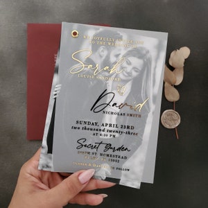May include: A translucent wedding invitation card featuring a black and white photograph of a couple, gold foil lettering for the names Sarah Louise Sandford and David Nicholas Smith, a gold eyelet, and printed details for Sunday, April 23rd, 2023.