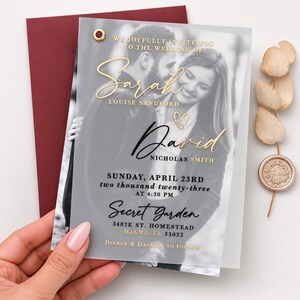 May include: A translucent wedding invitation card featuring a black and white photograph of a couple, gold foil lettering, and a gold eyelet. The text reads: We joyfully invite you to the wedding of Sarah Louise Sandford and David Nicholas Smith.