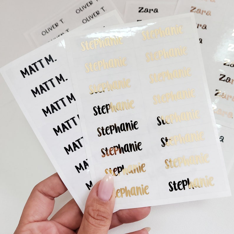 May include: A sheet of white labels with gold and black lettering. The labels are for names, including "Matt M." and "Stephanie".
