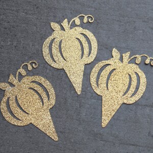 Peut inclure: Trois d&eacute;coupes de papier en forme de citrouille dor&eacute;es &agrave; paillettes. Chaque citrouille a une tige et une vigne. Les citrouilles ont la forme d'un cornet de glace.