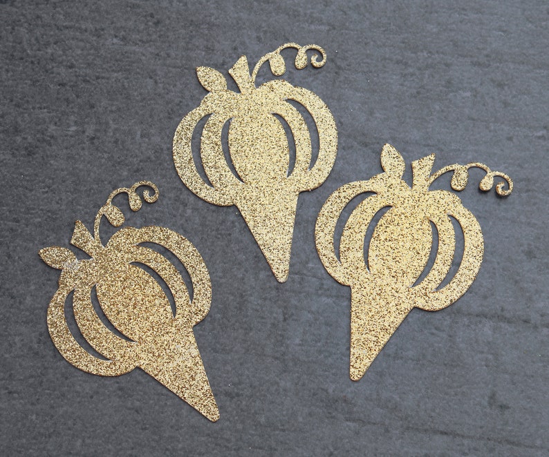 Peut inclure: Trois d&eacute;coupes de papier en forme de citrouille dor&eacute;es &agrave; paillettes. Chaque citrouille a une tige et une vigne. Les citrouilles ont la forme d'un cornet de glace.