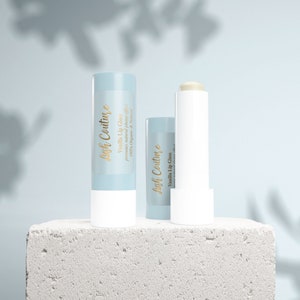 Puede incluir: Dos tubos de brillo labial de vainilla, uno con una etiqueta azul que dice "Lish Couture Brillo labial de vainilla promueve un efecto de relleno natural 100% org&aacute;nico y natural" y el otro con una etiqueta blanca que dice "Lish Couture Brillo labial de vainilla".