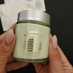 May include: A white jar with a green lid and a gold label listing the ingredients: Rose Centifolia Flower Water, Aqua, Lauryl Betaine, Acrylates/Beheneth-5, Methacrylate Copolymer, Triethanolamine, Phenethyl Alcohol, Phenoxyethanol, Sodium PCA, Vitis Vinifera Seed Extract.