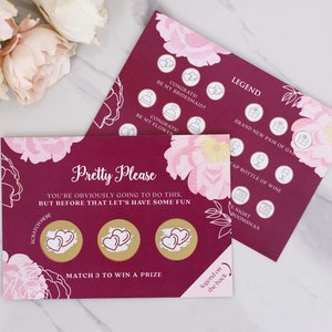 May include: A pink and burgundy card with a floral design. The card has three gold circles with hearts inside. The text on the card reads "Pretty Please You're obviously going to do this. But before that let's have some fun. Scratch here Match 3 to win a prize Legend on the back".