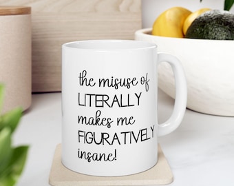 May include: White ceramic mug with the text "the misuse of LITERALLY makes me FIGURATIVELY insane!" in black script. The mug sits on a beige coaster. A white handle is visible on the right side of the mug.