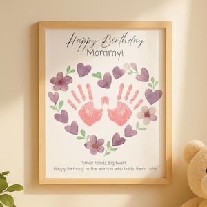 Może przedstawiać: Oprawiony wydruk z napisem "Happy Birthday Mommy!" przedstawia sercowaty wzór z fioletowych serc, kwiatów i różowych odcisków dłoni. Zawiera również tekst "Small hands, big heart".