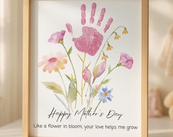 May include: A framed print with a light wood frame. The artwork features a pink handprint above a watercolor floral arrangement. The text reads "Happy Mother's Day" and "Like a flower in bloom, your love helps me grow."