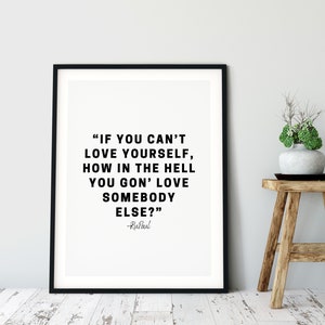 May include: Black and white typography print with a quote by RuPaul: "If you can't love yourself, how in the hell you gon' love somebody else?" The print is framed in a black frame and is displayed on a white wall.