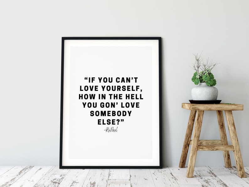 May include: Black and white typography print with a quote by RuPaul: "If you can't love yourself, how in the hell you gon' love somebody else?" The print is framed in a black frame and is displayed on a white wall.