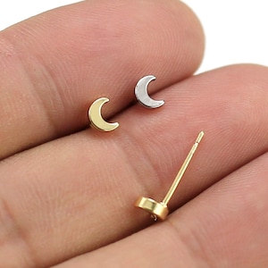 May include: A pair of crescent moon earrings, one gold and one silver, on a person's finger.