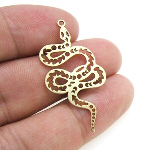Op de afbeelding: Gouden metalen hanger in de vorm van een slang met een uitgesneden ontwerp. De slang is opgerold met zijn staart in zijn mond.