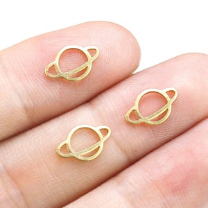 May include: Three gold-colored metal charms shaped like a planet with a ring around it.