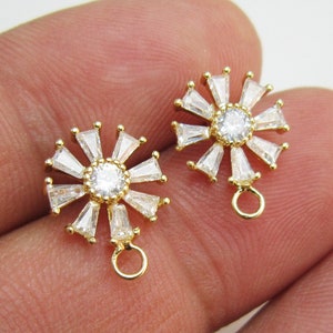 May include: A pair of gold-tone earring charms with a round, clear crystal center surrounded by smaller clear crystals. Each charm has a gold loop for attaching to a chain or earring.