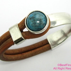May include: A brown leather bracelet with a silver metal band and a blue gemstone. The bracelet is adjustable and has a simple design.