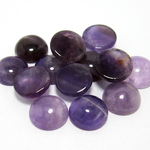 Könnte beinhalten: Eine Gruppe von 12 runden, cabochon geschliffenen Amethyst-Edelsteinen in verschiedenen Violetttönen. Die Steine sind glatt und poliert, mit einem glänzenden Finish.
