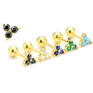 Op de afbeelding: Een set van zes gouden oorbel studs met een ontwerp met drie stenen. De stenen zijn in verschillende kleuren, waaronder zwart, wit, blauw, groen en turquoise.