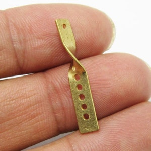 Könnte beinhalten: Ein goldfarbener Metallverbinder mit einer gedrehten Form und fünf Löchern. Der Verbinder ist etwa 3,8 cm lang.