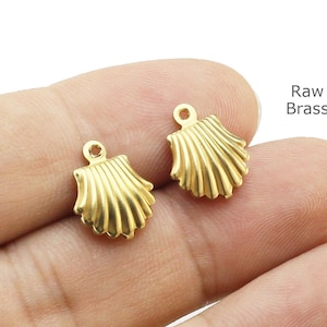 Op de afbeelding: Twee kleine, goudkleurige schelpenbedels. Elke bedel heeft een lus aan de bovenkant om aan sieraden te bevestigen. De bedels zijn gemaakt van onbewerkt messing. Het schelpenontwerp heeft gedetailleerde ribbels.
