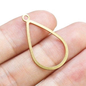 Op de afbeelding: Een gouden metalen hanger in de vorm van een traan met een lus aan de bovenkant om een ​​ketting of koord aan te bevestigen.