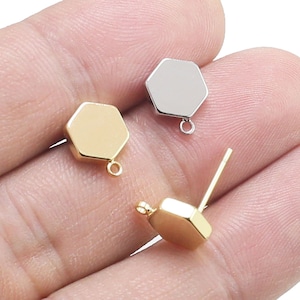 Puede incluir: Tres abalorios hexagonales de metal con anillas de salto. Dos abalorios son dorados y uno es plateado.