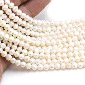 Puede incluir: Una hebra de perlas de agua dulce blancas, cada perla es redonda y lisa. Las perlas están enhebradas en un hilo transparente y están listas para ser utilizadas en la elaboración de joyas.