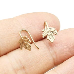 May include: A pair of gold leaf dangle earrings with a simple design. The earrings are made of metal and have a hook closure.