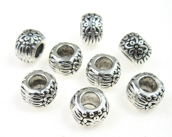 May include: Ten silver-toned metal beads with a decorative floral design. The beads are round and have a hole in the centre for stringing.