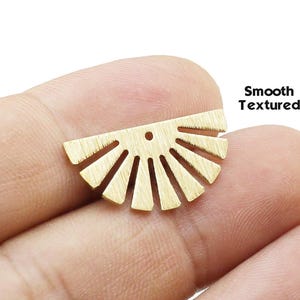Peut inclure: Une breloque en métal doré en forme de demi-cercle avec des rayons de soleil rayonnants. La pièce présente un petit trou au centre supérieur pour la fixation et possède une finition brossée avec le texte Smooth Textured imprimé à côté.